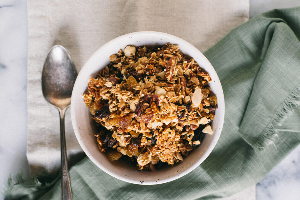 Top down photo of a bowl full of homemade granola with a silver spoon on green and linen napkins