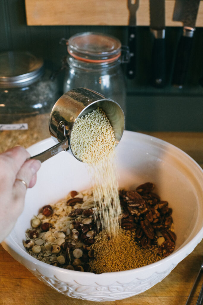 Photo of a measuring cup of millet being poured into a bowl of homemade granola ingredients