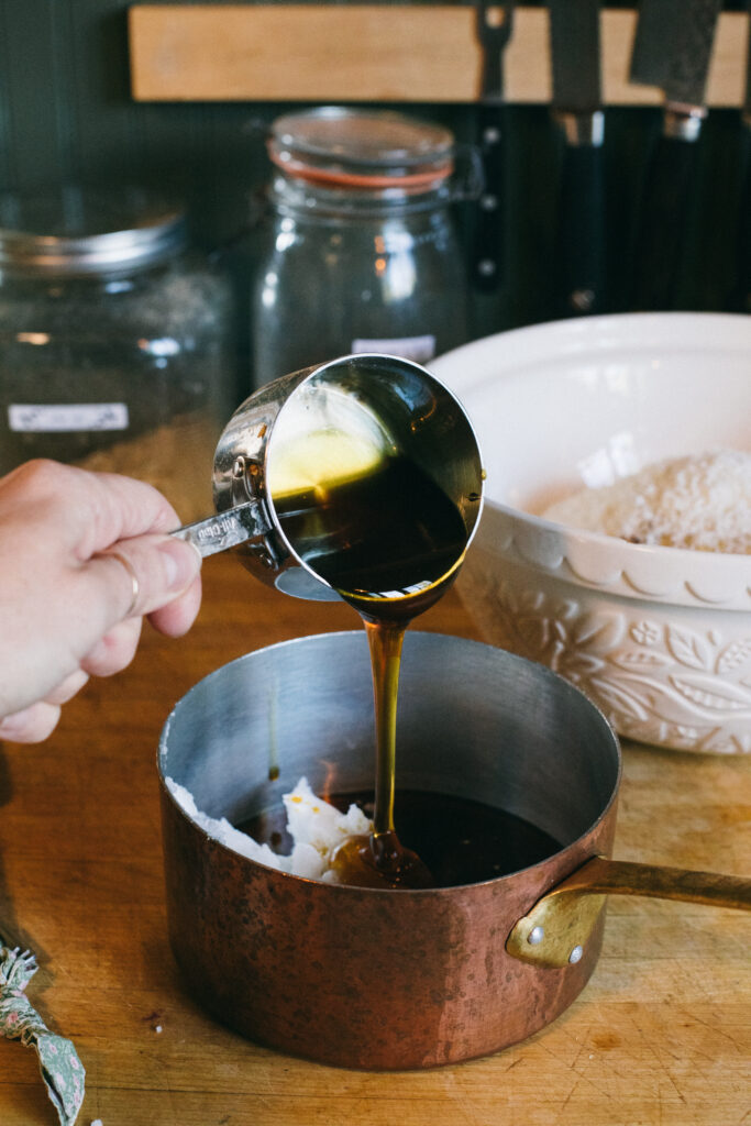 Photo of maple syrup being poured into a copper saucepan from a measuring cup for homemade granola