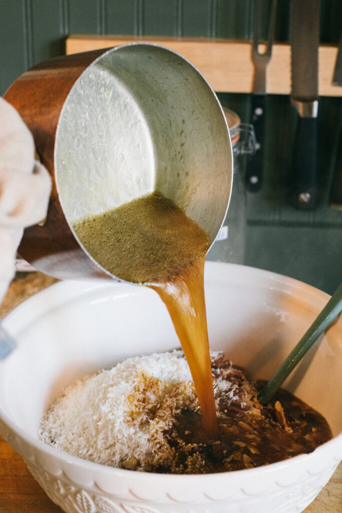 Photo of a pot of maple drizzle liquid being poured over a bowl of homemade granola