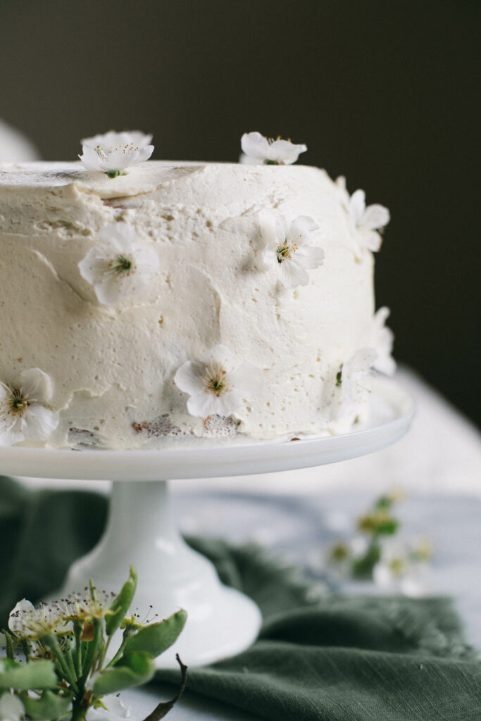 Photo of a white Einkorn Sponge Cake covered in cherry blossoms on a white cake stand