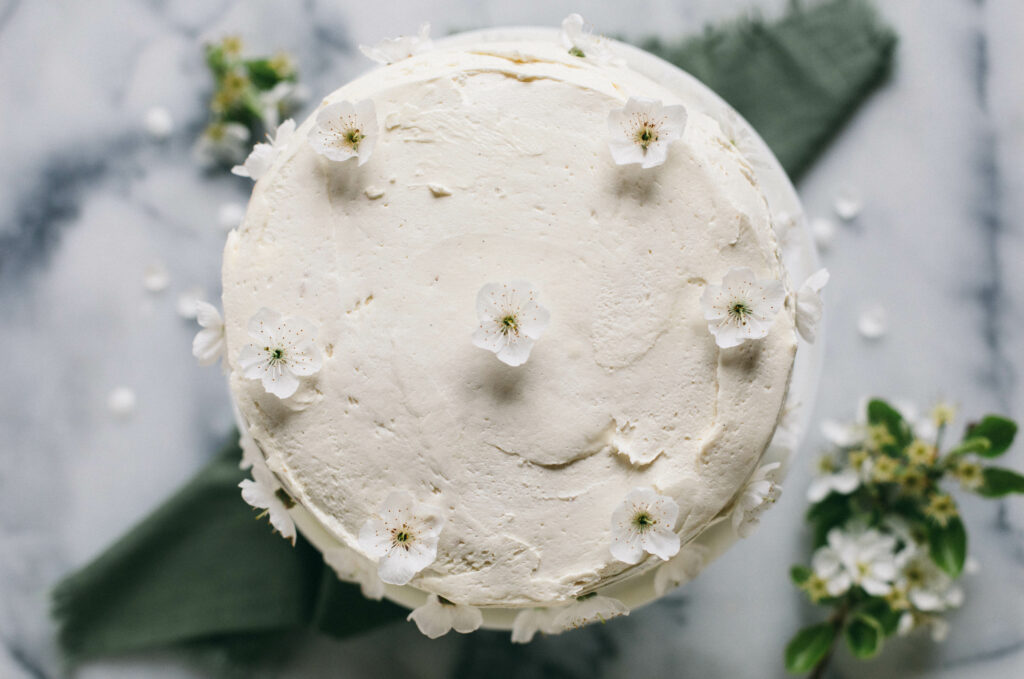 Overhead photo of a white Einkorn Sponge Cake covered in cherry blossoms