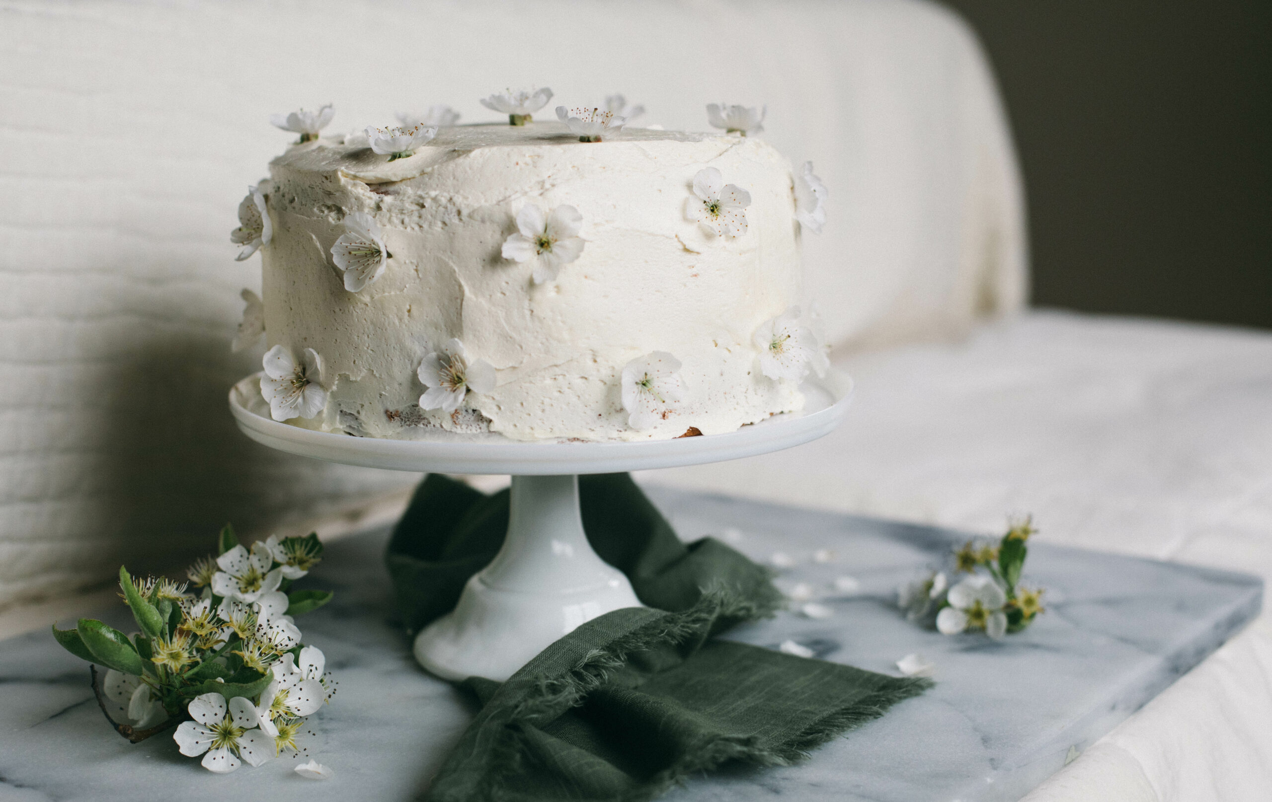 Image of a white Einkorn Sponge cake on a white cake stand with orchard blossoms