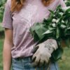 Image in a Potager Online Lilac Gardening Tee holding lilacs and wearing gardening gloves