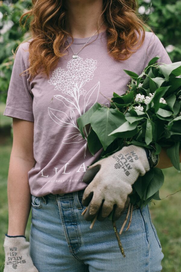 Image in a Potager Online Lilac Gardening Tee holding lilacs and wearing gardening gloves