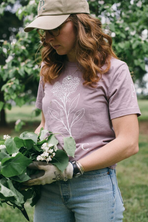 Image in a Potager Online Lilac Gardening Tee holding lilacs and wearing gardening gloves