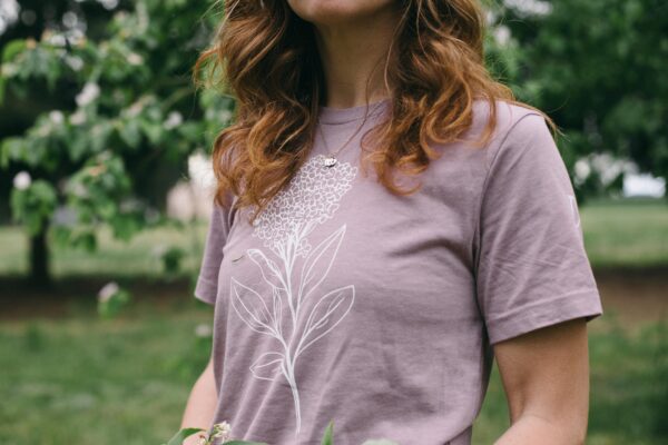 Image in a Potager Online Lilac Gardening Tee holding lilacs and wearing gardening gloves