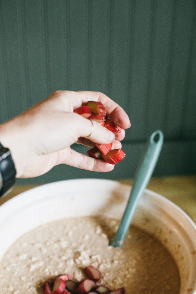 Photo of a hand tossing sliced Rhubarb into a Sourdough Rhubarb Oatmeal Bake