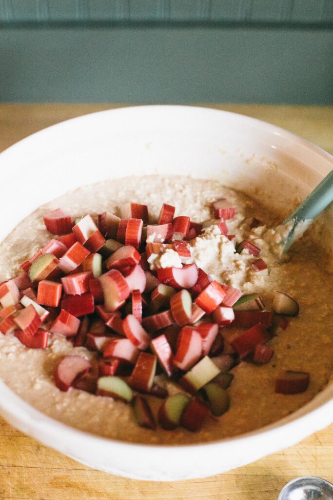 Photo of rhubarb added to a white bowl of Sourdough Rhubarb Oatmeal Bake before being baked