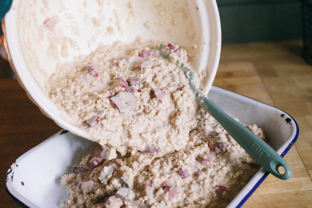 Photo of the batter of a Sourdough Rhubarb Oatmeal Bake being poured into the enamel baking dish for baking