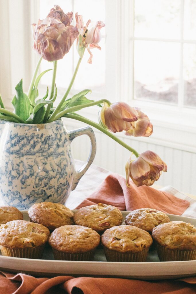 Image of a tray of rhubarb muffins with a spongeware pitcher of tulips in front of a window