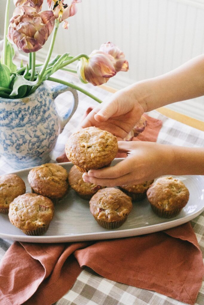 Image of a tray of rhubarb muffins with a child's hands holding a fresh muffin