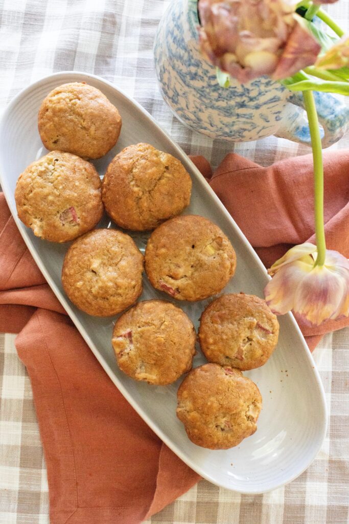 Image of a tray of rhubarb muffins on a gingham tablecloth with a spongeware pitcher of tulips