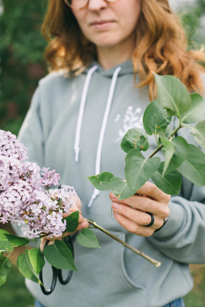 Image of a woman removing the leaves from a steam of lilacs for making a flower arrangement
