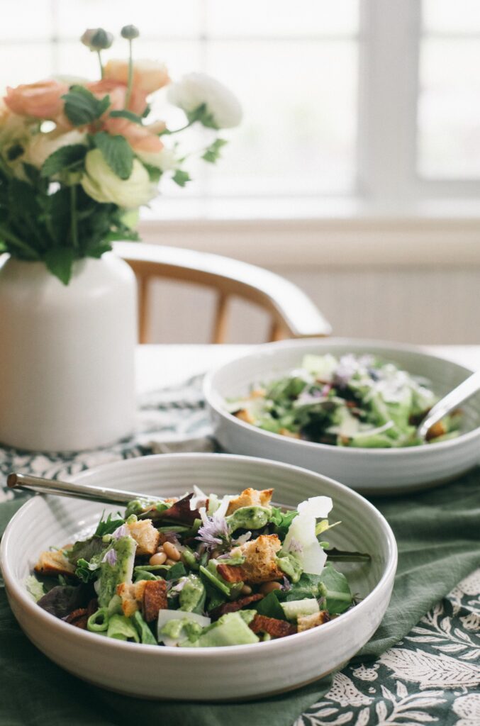 Image of two Garden Chop Salads sitting on a table with flowers and green napkin with Green Goddess Dressing
