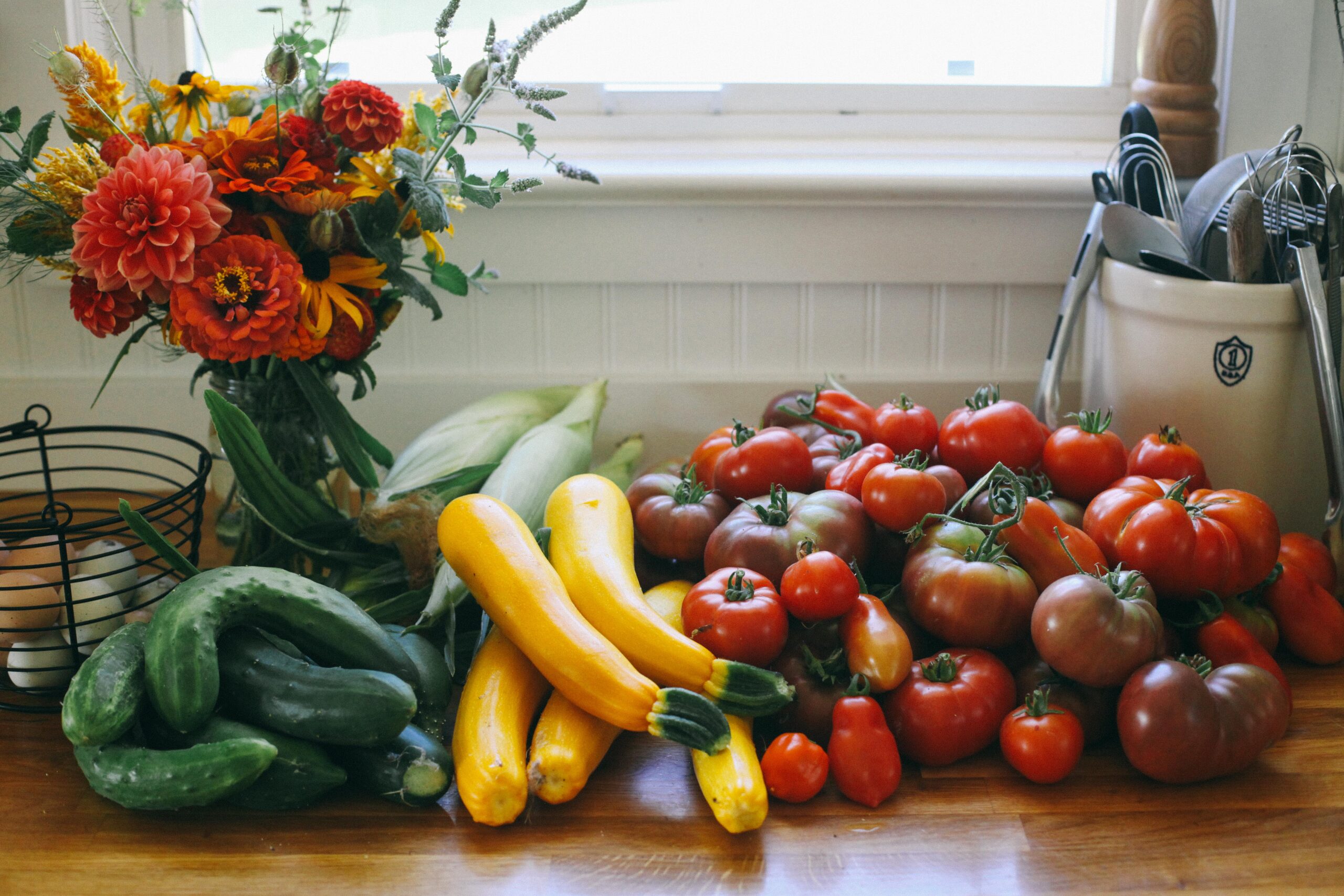 Photo of garden vegetables like cucumbers, summer squash, zucchini and tomatoes on the counter in a farmhouse kitchen