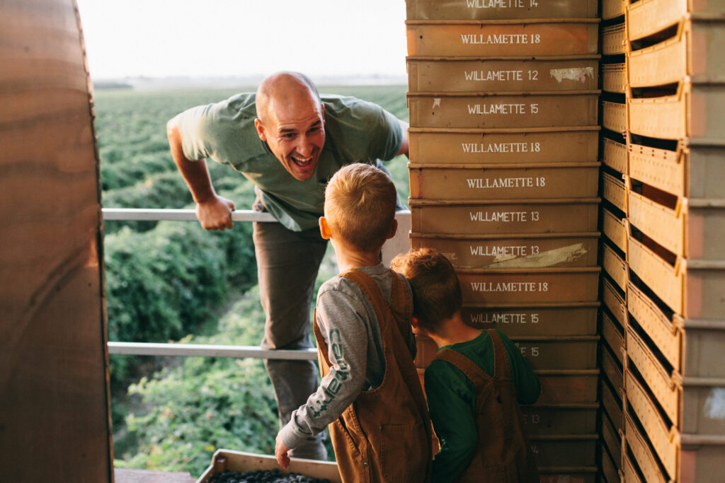 Image of an Oregon blackberry farmer on a berry picker talking to two little farmer boys
