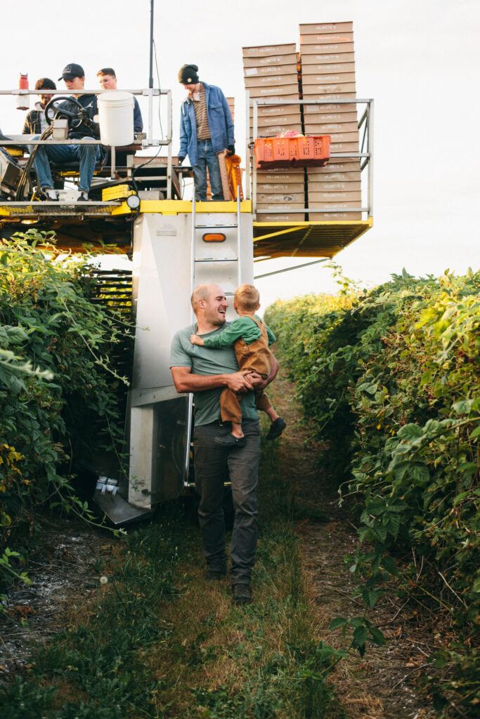 Image of a farmer holding his little boy in front of a berry picking machine on an Oregon berry farm for fantastic desserts
