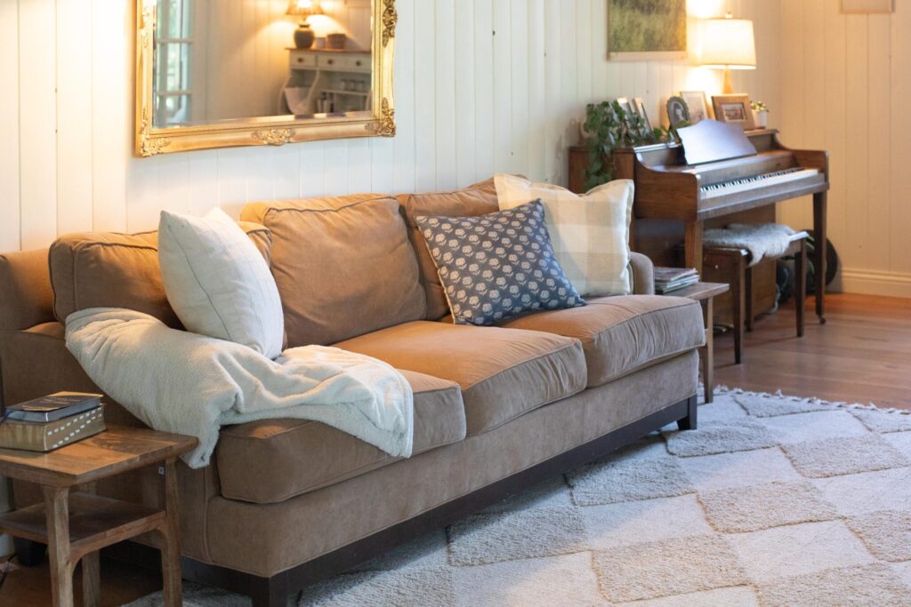 Image of a secondhand sofa and antique mirror with cozy throw pillows and blankets in a Swedish Cottage living room