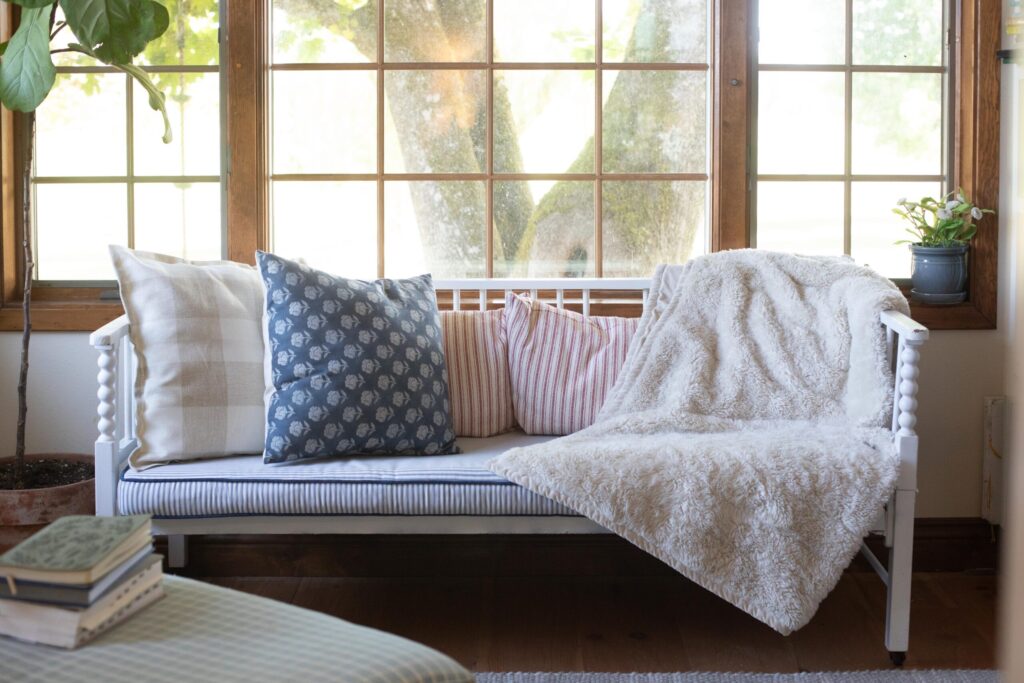 Image of a Swedish Cottage Sunroom filled with secondhand furniture, cozy blankets and throw pillows