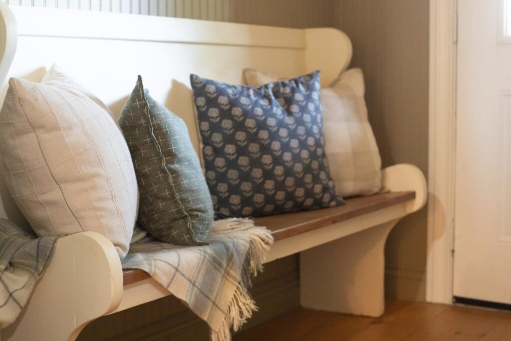 Image of a secondhand bench filled with cozy pillows and a thrifted throw blanket