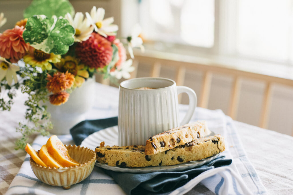 Image of an orange chocolate chip biscotti set out on a table with a cup of coffee