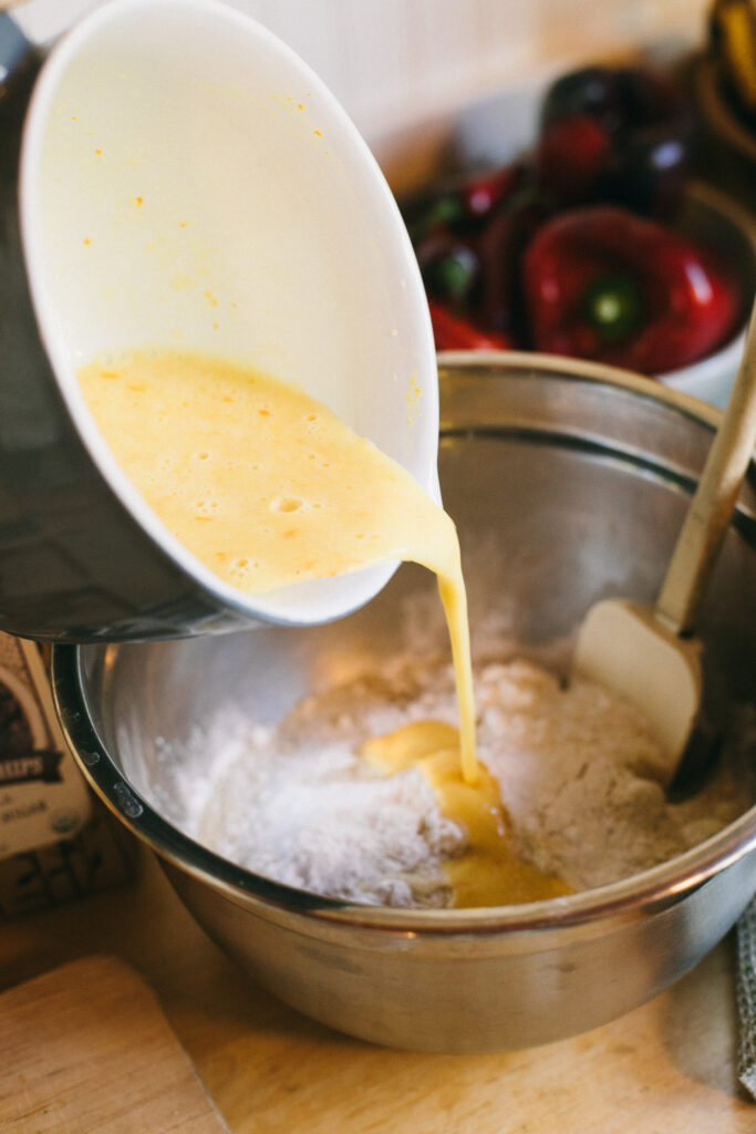 Image of a mixing bowl of eggs being poured into a mixing bowl of dry ingredients